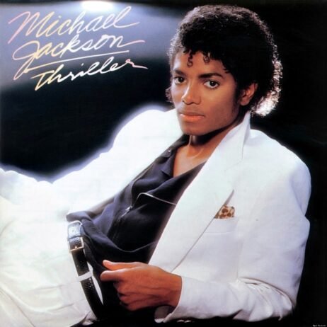 This is the album cover for Michael Jackson - Thriller. Michael Jackson poses in a stylish white suit with a black shirt underneath, reclining with a relaxed yet confident expression. His curly hair is perfectly styled, and the lighting gives the image a soft glow, highlighting his iconic look. The handwritten album title "Thriller" and his name appear in the upper left corner.