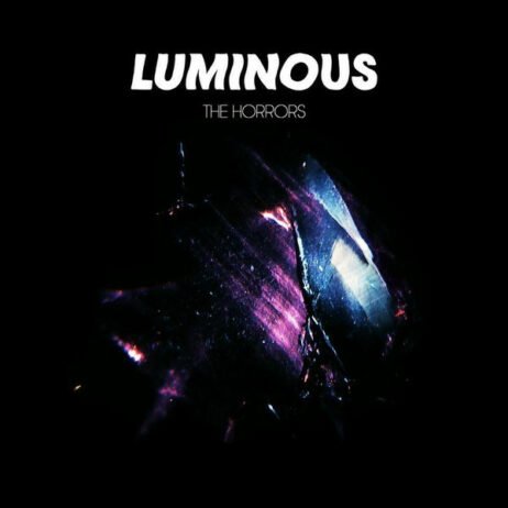 This is the album cover for "Luminous" by The Horrors. The design features a dark, abstract background with streaks of purple and blue light that create a glowing, almost crystalline effect. The album's title, "LUMINOUS," is prominently displayed in a bold, white font at the top, with the band's name, "THE HORRORS," written just below it in a more delicate and subtle typeface.