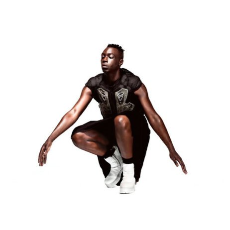 The image depicts a person in a dynamic, crouching pose against a plain white background. They are dressed in a unique, stylish outfit, featuring a sleeveless top with intricate details and a skirt or long shorts, paired with high white boots.