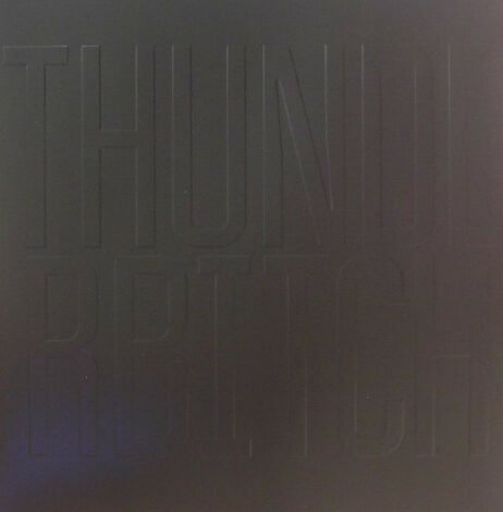 The image has a dark, monochromatic design with subtle text that reads THUNDERBITCH. The text is in faint grey.