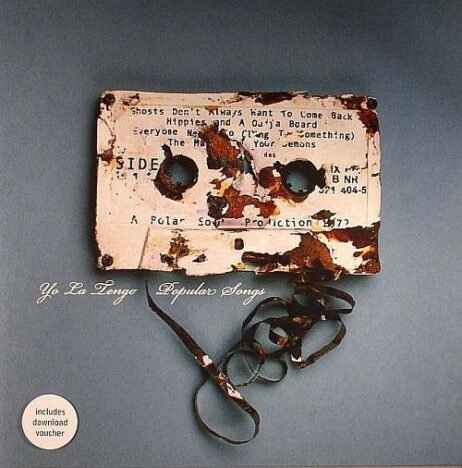 The image is the album cover for "Popular Songs" by Yo La Tengo. The cover features a worn and partially destroyed cassette tape with its magnetic tape unspooled.
