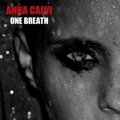 This image is the album cover for "Anna Calvi" in red. The title "One Breath" is below the artist's name in white. The cover features a close-up of Anna Calvi's face, with a dramatic, intense focus on her eye. The cover is in a monochromatic and high-contrast style.