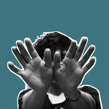 The image is the album cover for "I can feel you creep into my private life" by Tune-Yards. The cover features a stylized photo of someone holding their hands up in front of their face, with a teal background.