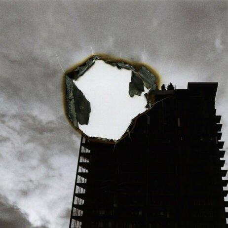 The image is the album cover for Jo Passed's "Their Prime." The cover features a black-and-white photo of a tall, dark building against a cloudy sky, with a striking visual element: a large burn or tear at the center of the image, exposing an abstract, empty space within. The burnt edge is detailed, with shades of orange and brown.
