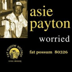 The image is of the album cover for Asie Payton's "Worried", released by Fat Possum Records. The cover features a sepia-toned photograph of Asie Payton sitting with a microphone, wearing a cap in the top left corner. The text is presented in a simple, bold style, with "Asie Payton" written in yellow lowercase letters, and the title "Worried"in white just below it. The Fat Possum Records logo, along with "Oxford, Mississippi," is placed in the lower left corner.