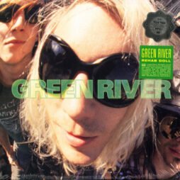 This image is the album cover for "Rehab Doll" by Green River. It features a close-up, fisheye-lens photograph of one of the band members, with blonde hair and large, round black sunglasses, creating a distorted, dynamic effect. Two other members are partially visible in the background, also wearing sunglasses. The band's name, "Green River," is written prominently across the center in bold, bright green letters. There is a sticker on the upper right corner that includes the album title, "Rehab Doll," along with other details.