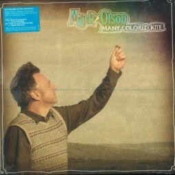 The image is the album cover for Mark Olson - Many Colored Kite. The cover shows Mark Olson standing outdoors in a pastoral setting, gazing upwards with his arm raised as if he's about to release something into the sky. The design has a soft, vintage aesthetic, with muted colours and a subtle texture overlay. The album title "Many Colored Kite" is written in a whimsical, playful font next to the artist's name "Mark Olson."