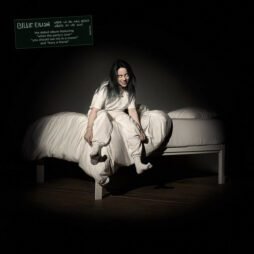 The image is the album cover for "When We All Fall Asleep, Where Do We Go?" by Billie Eilish. It features Billie Eilish sitting on the edge of a white bed in a dimly lit room, dressed in all white with her hair partially covering her face. The lighting creates a spotlight effect, emphasizing her eerie smile and shadowy surroundings. In the top left corner, there is a green sign with text that includes the album's title and features.