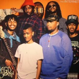 The album cover shows the members of the band The Internet standing together against an orange background. Each member has a distinct style, from casual to cool. Syd, the lead vocalist, stands at the front in a white T-shirt with a calm expression. The bandâ€™s name, "The Internet," is written in the top right corner, while the album title "Ego Death" is handwritten in the bottom left.