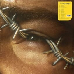 The album cover features a close-up of a human eye with barbed wire wrapped around the brow and eyelid, creating a dramatic and intense visual. The barbed wire symbolizes restriction or pain, contrasting sharply with the delicate skin around the eye. A yellow label with text is placed in the top right corner, listing track information or details.