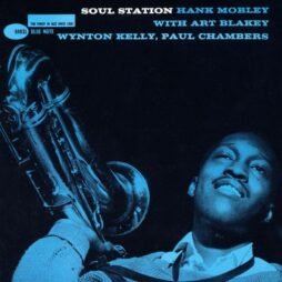 The image is the album cover for "Soul Station" by Hank Mobley. It features a blue-tinted photograph of Hank Mobley holding his saxophone. Mobley is smiling and looking upwards. The album title, artist's name, and names of other featured musicians (Art Blakey, Wynton Kelly, Paul Chambers) are printed in bold text at the top, with the Blue Note label logo on the left.