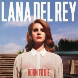 The album cover features Lana Del Rey standing against a clear blue sky. She has long, wavy auburn hair and wears a sheer white blouse with a high collar, looking directly at the camera with a confident, serene expression. The bold text at the top reads "LANA DEL REY" in large white letters, and the album title "BORN TO DIE" is placed at the bottom in red. The background shows a blurred suburban setting.