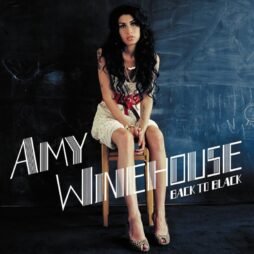 The image is the album cover for "Back to Black" by Amy Winehouse. It features a photograph of Amy Winehouse sitting on a wooden chair against a dark chalkboard background, wearing a white dress with a red belt. Her long, black hair is loose and wavy, and she looks directly at the camera with a melancholic expression. The artist's name "Amy Winehouse" is written in bold, stylized white letters across the image, with the album title "Back to Black" beneath it.