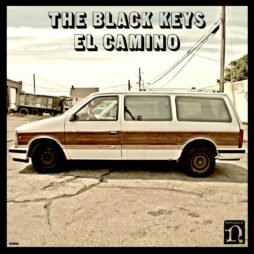 A retro-styled cover features an old beige minivan with faux wood paneling parked on a cracked asphalt lot. The vehicle is captured in a side profile against a backdrop of a run-down industrial area. The album title, "El Camino," and the band name, "The Black Keys," are written in bold, black, uppercase letters across the top, creating a vintage yet raw aesthetic.