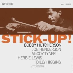 The album cover features a close-up image of Bobby Hutcherson playing the vibraphone in an intense, focused expression. The title "STICK-UP!" is prominently displayed in large, bold orange letters across the center. Below, in smaller black and gray text, the artist's name, Bobby Hutcherson, is followed by the names of the featured musicians: Joe Henderson, McCoy Tyner, Herbie Lewis, and Billy Higgins.