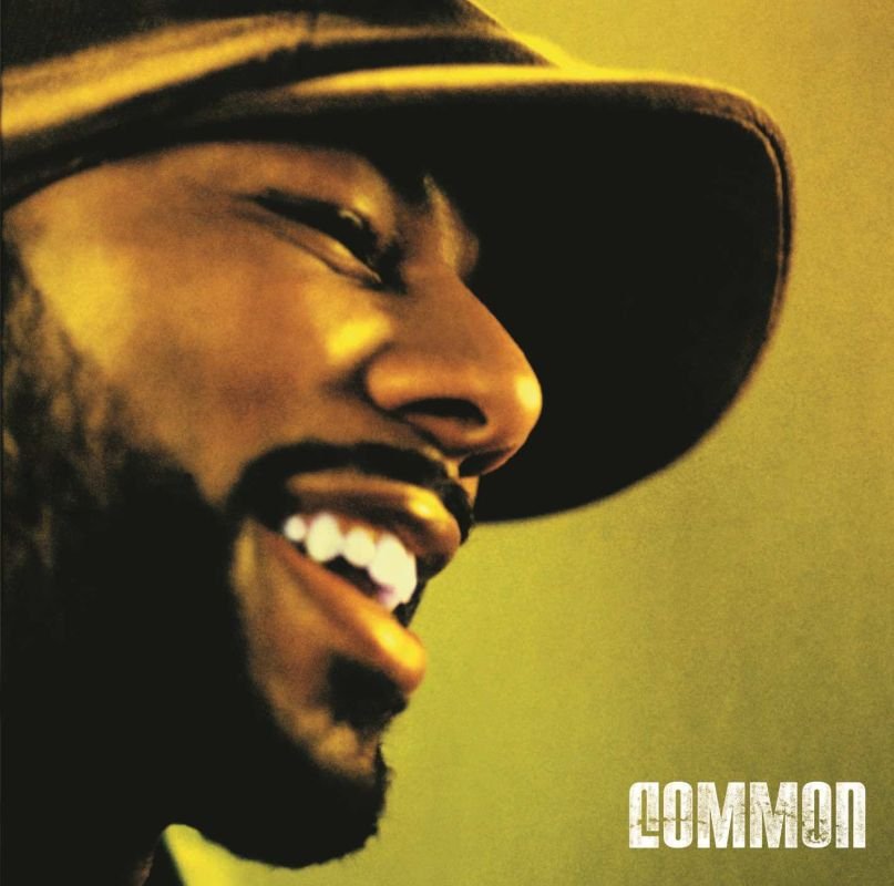 The album cover features a close-up of Common smiling, captured in warm golden light. His face is partially covered by a wide-brimmed hat, casting a soft shadow. The soft focus and glow add a serene and joyful tone to the image. The artist's name "Common" appears in bold, white text at the bottom right.