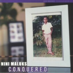 The image is the album cover for "C.O.N.Q.U.E.R.E.D" by Nini Maluks. It features a photograph of a framed picture showing a young boy in a light pink outfit standing outdoors beside a bush. The frame is positioned slightly at an angle against a blurred background. The artist's name, "NINI MALUKS," and the album title, "C.O.N.Q.U.E.R.E.D," are displayed in bold white text at the bottom.