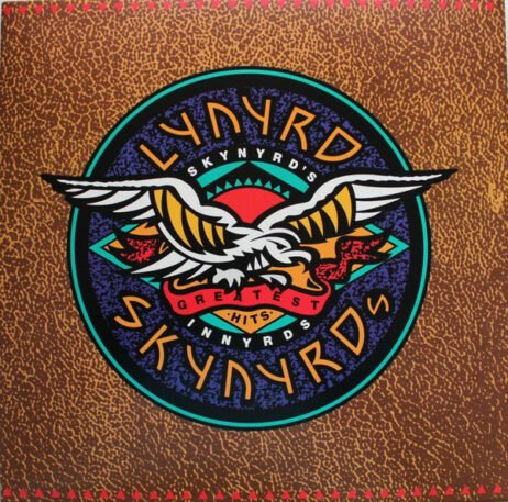 The album cover for Lynyrd Skynyrd's Greatest Hits features a stylized circular emblem with a large eagle spreading its wings in the center. The eagle is set against a vibrant background with red, blue, and green hues. The band's name, "Lynyrd Skynyrd," is prominently displayed in a bold, colorful font encircling the eagle, with "Greatest Hits" written across the bottom. The background has a rustic, textured pattern.