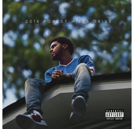 The image is the album cover for "2014 Forest Hills Drive" by J. Cole. It shows J. Cole sitting on the roof of a house, looking contemplatively into the distance. He is wearing a blue sports jersey, jeans, and sneakers. The background is blurred, featuring green foliage, with the album title in white text above. A "Parental Advisory Explicit Content" label is in the bottom right corner.