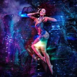 The album cover features a vibrant, cosmic scene with a woman lying gracefully amidst a galaxy-like background. Her body is adorned with shimmering colors, blending seamlessly with the stars and nebulae surrounding her. The colors are predominantly blue, purple, and pink, giving an ethereal and otherworldly vibe. Vertical text appears along her body, adding a futuristic touch to the composition.