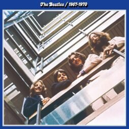 The album cover for The Beatles 1967â€“1970 features an iconic photograph of The Beatles taken from a low angle. The membersâ€”John Lennon, Paul McCartney, George Harrison, and Ringo Starrâ€”are looking down from a balcony. The shot creates a symmetrical, geometric effect with the building's structure. The album title is presented at the top in a simple white font against a blue background.