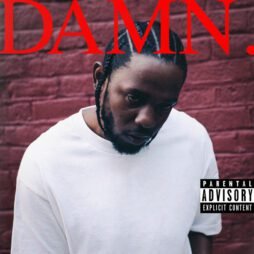 The image is the album cover for "DAMN." by Kendrick Lamar. It features Kendrick Lamar wearing a plain white t-shirt, looking down with a serious expression, set against a red brick wall. The album title "DAMN." is written in bold, large red capital letters at the top. A "Parental Advisory: Explicit Content" label is displayed in the bottom right corner.