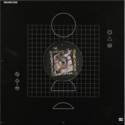 The image shows an album cover from the "Drumcode" label. The design features a dark black background with a grid pattern in the center. Inside the grid is a circular image that appears to be an abstract, fragmented piece of artwork, featuring various colors and textures, including metallic and organic elements. The circular image is surrounded by a chain-like border.