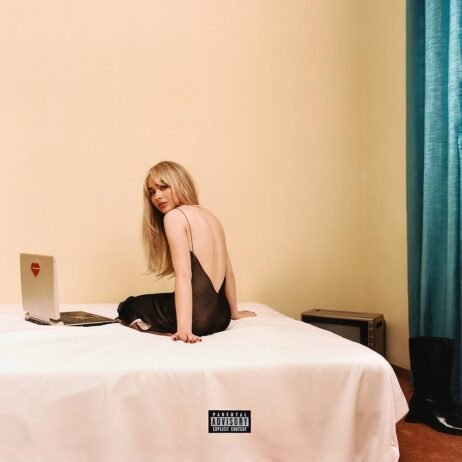 This is the album cover for Sabrina Carpenter - Emails I canâ€™t send. A woman with long blonde hair sits on a bed in a dimly lit room. She is wearing a black, backless dress and looking over her shoulder at the camera. Beside her is a laptop with a red heart sticker. The room features minimalist decor with plain beige walls and teal curtains.