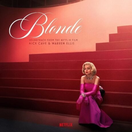 The image is the cover for the soundtrack of the Netflix film "Blonde," composed by Nick Cave and Warren Ellis. The cover features a woman, resembling Marilyn Monroe, seated on a grand red staircase. She is dressed in a glamorous, bright pink gown with matching gloves, wearing a statement necklace and a classic blonde hairstyle. The title "Blonde" is written in elegant, cursive white text at the top left.