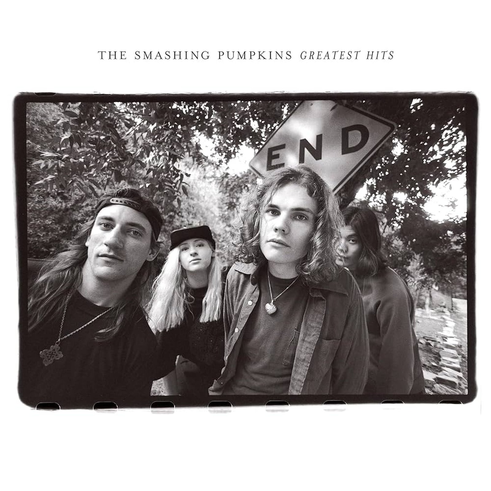 The album cover for The Smashing Pumpkins Greatest Hits and features a black-and-white photo of the band. The members stand close together in front of an "End" street sign. The image has a slightly grainy, vintage feel, and the band's grunge-era style is prominent. The album title is written in simple, small text at the top.
