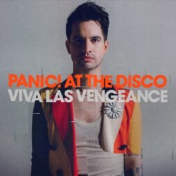 This is the album cover for Panic! At The Disco - Viva Las Vengeance. It features a man standing centre in an orange and yellow jacket with a white vest looking at the camera.